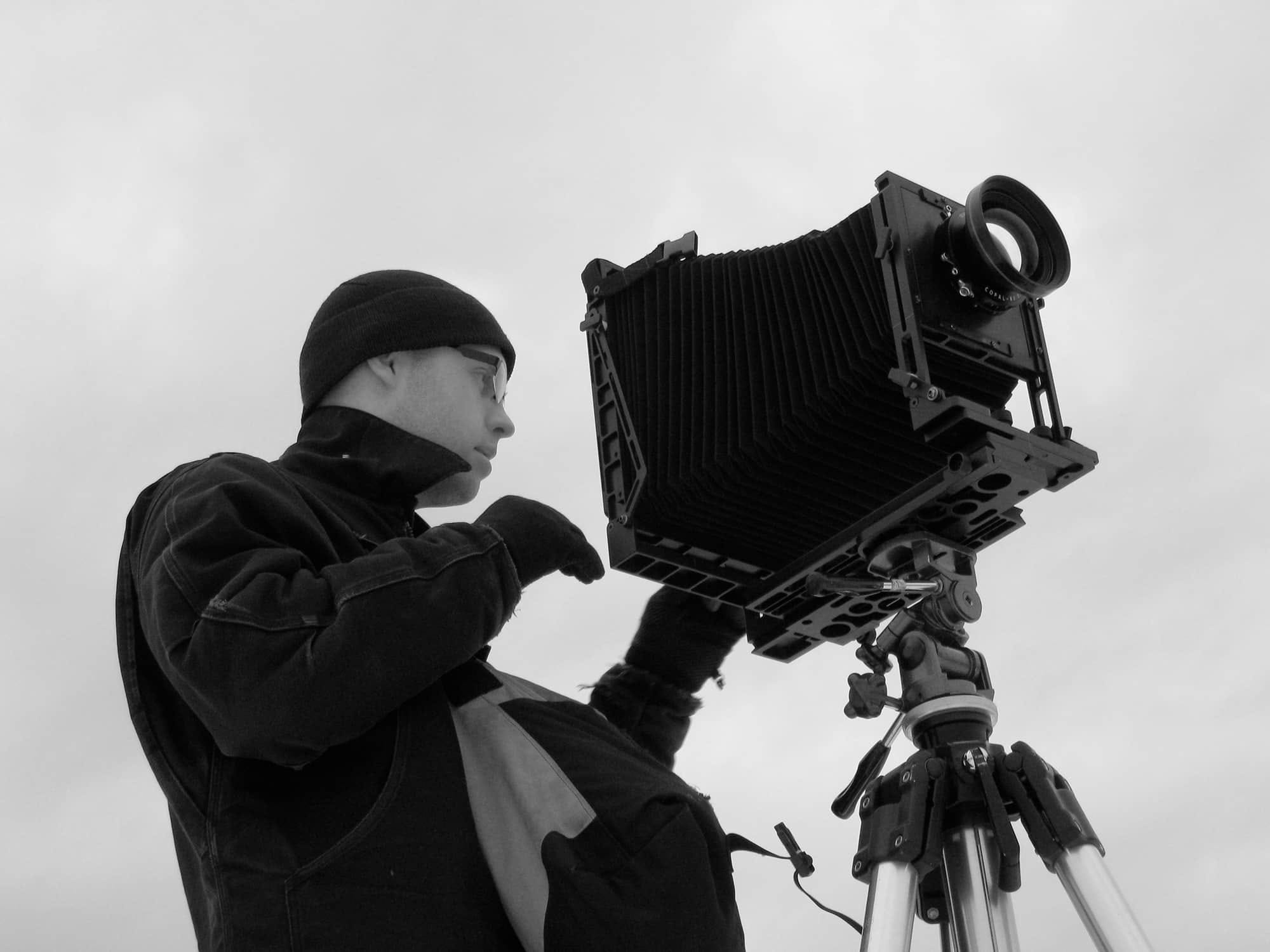 Adam Davies focusing a large metal view camera mounted on a tripod.
