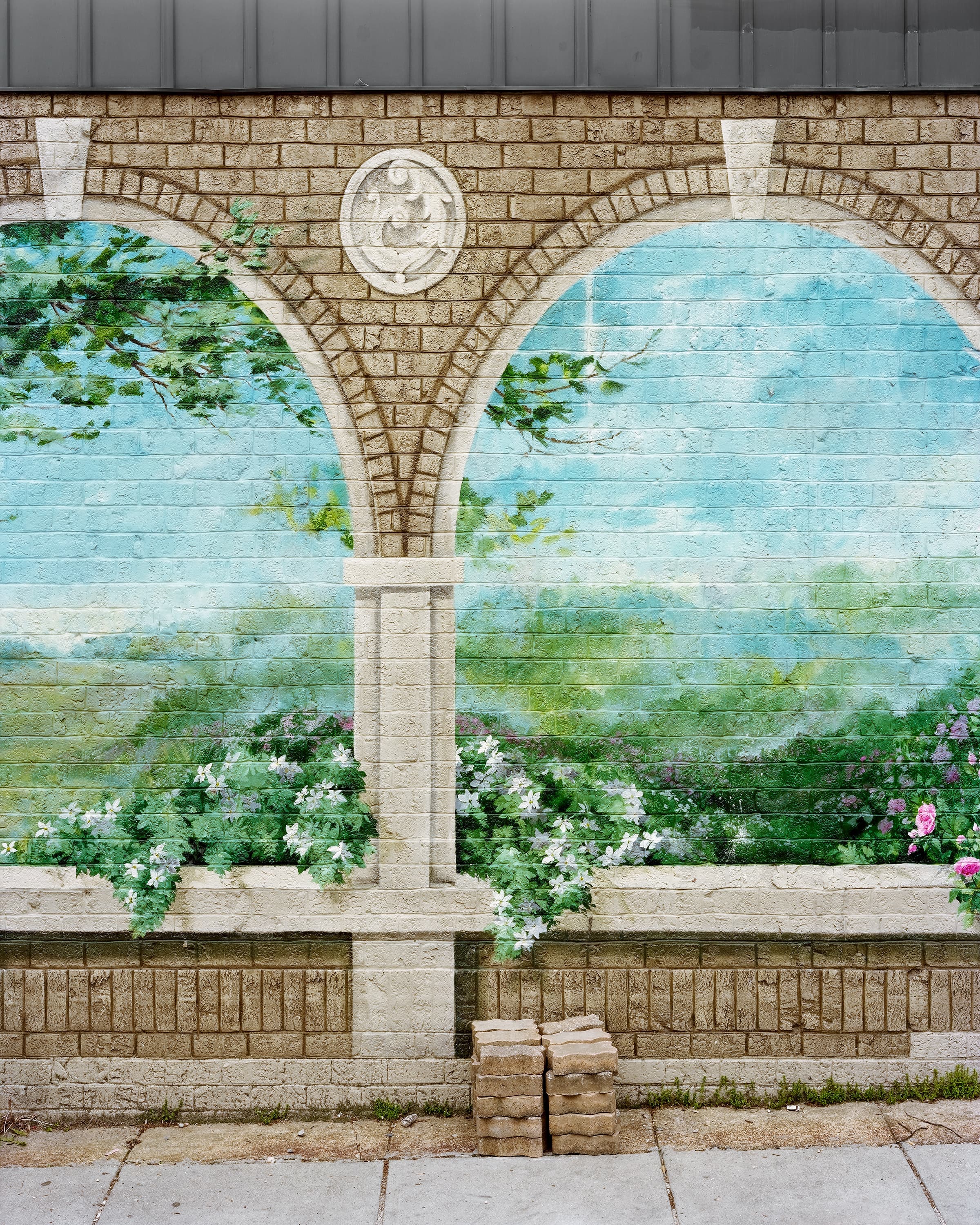 Painted mural of a series of arches overlooking flowers and landscape on an abandoned brick wall.