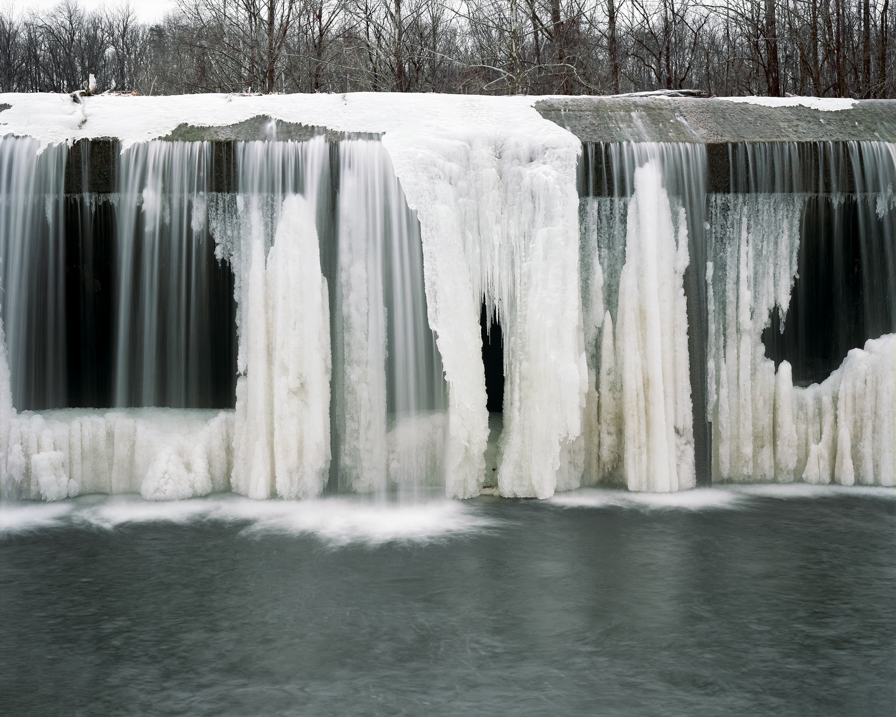 Water pouring over an ice covered dam.