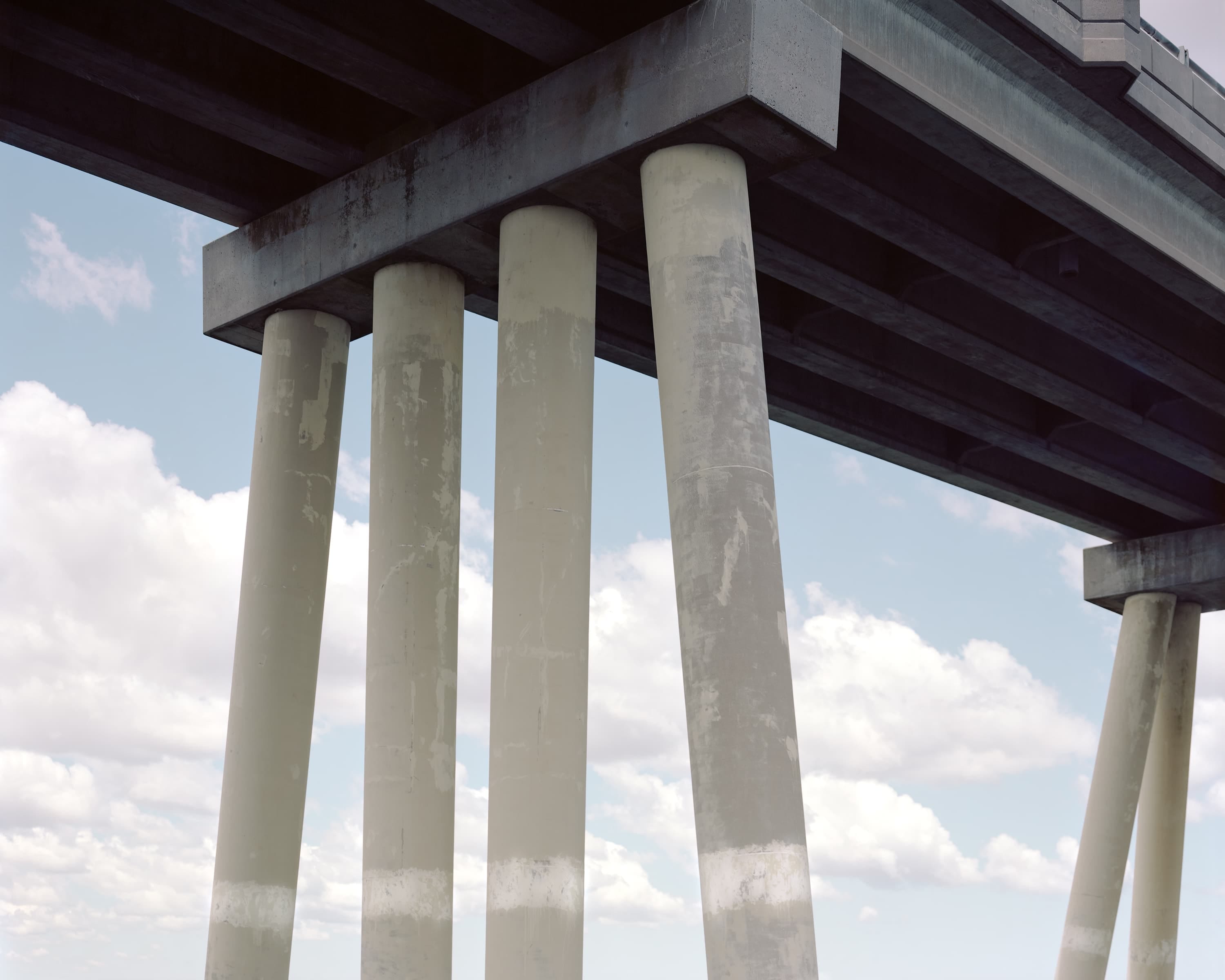 Bridge over water, its painted piers match the clouds in the background.