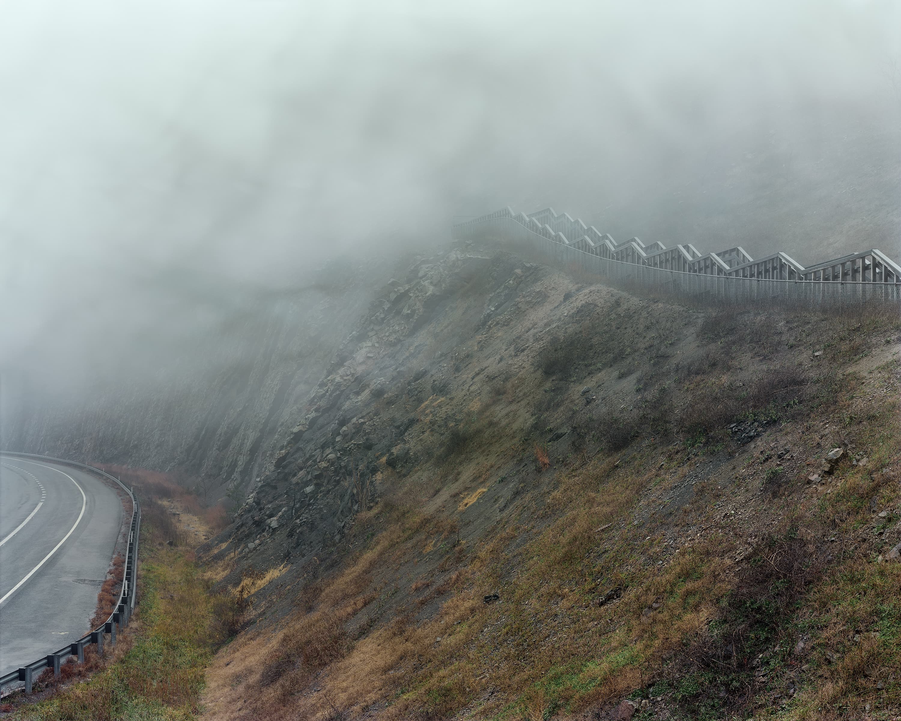 Fog covering a mountain pass with a pedestrian walkway going uphill.