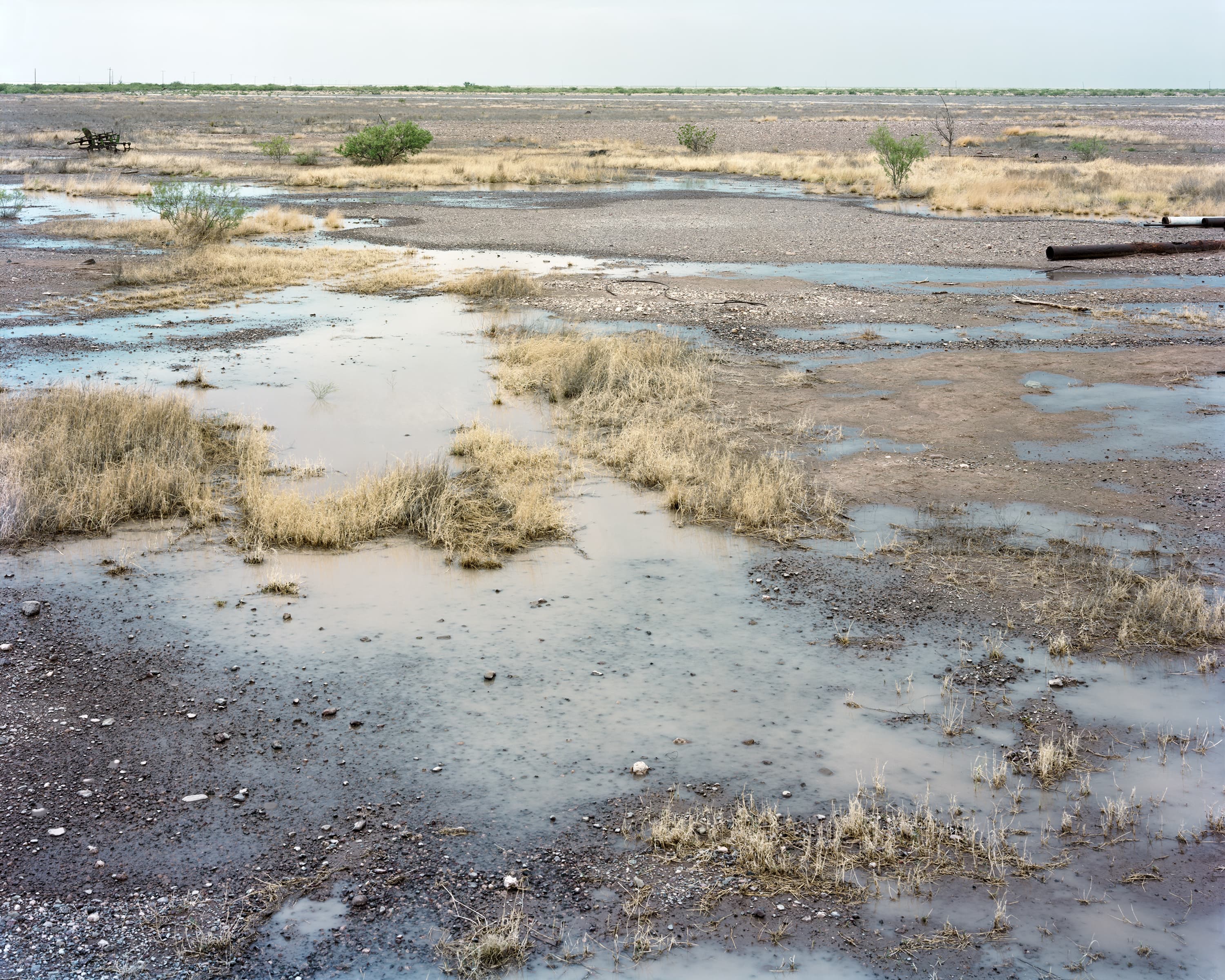 West Texan desert landscape and abandoned farming equipment after a rainstorm, this area has extremely elevated salt levels in the soil inhibiting growth and the puddles of water bring up the white, silvery salt particles to the surface.