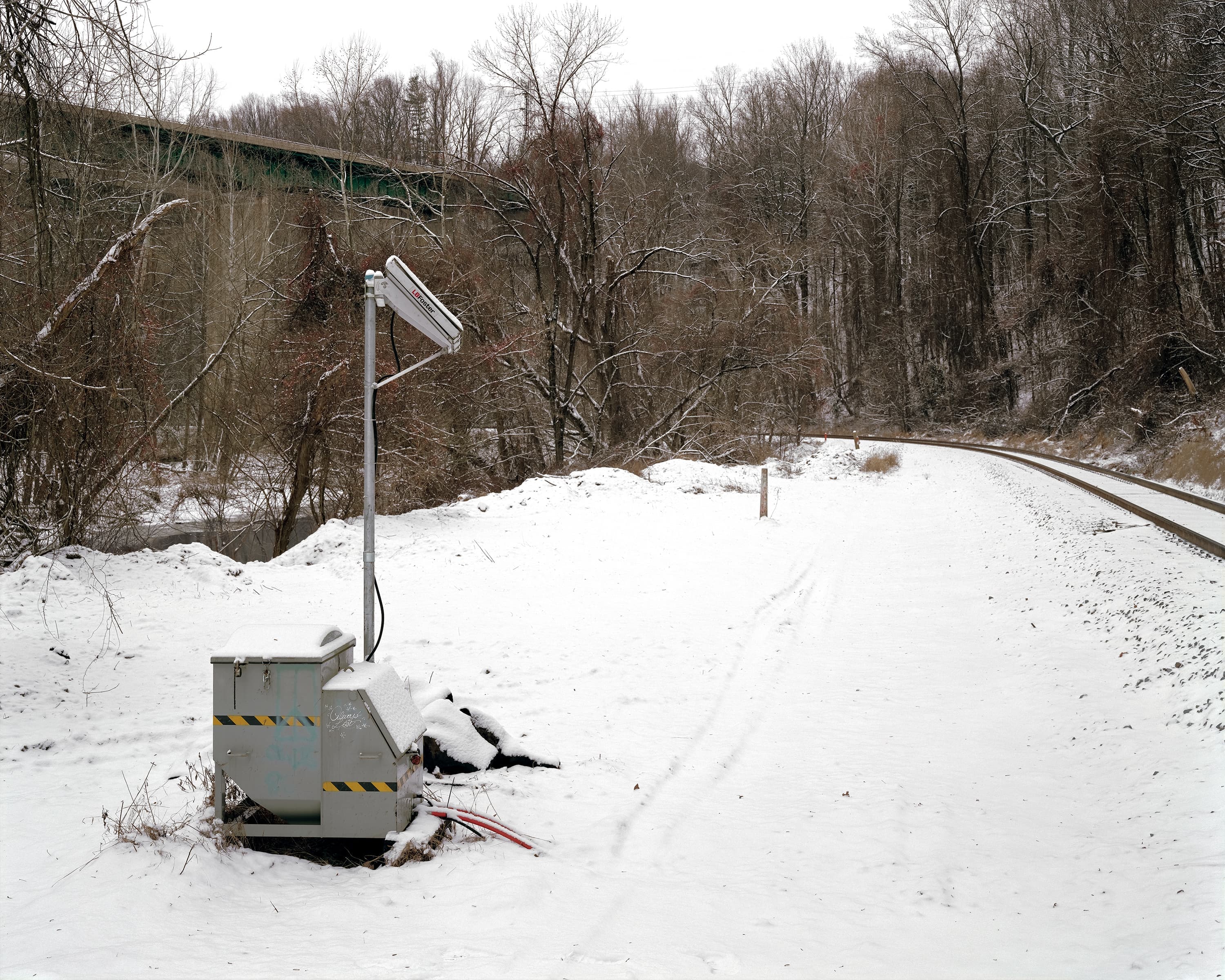 Winter landscape, on right a railway line runs through trees, on a signal box are hobo symbols and the graffiti 'always lost'.