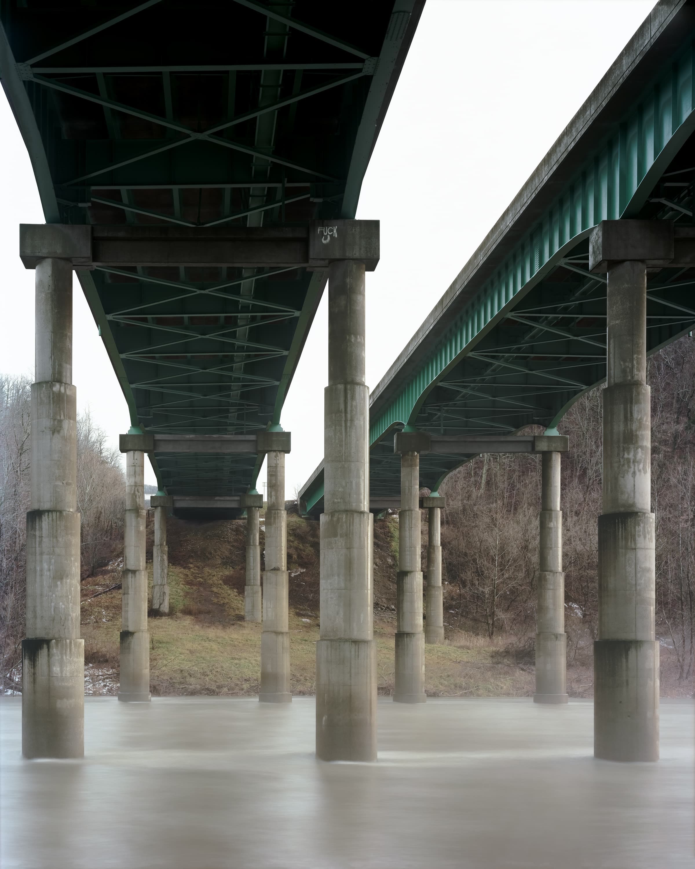 In a winter mist, text painted high in a difficult to access part of a pier on a highway bridge.