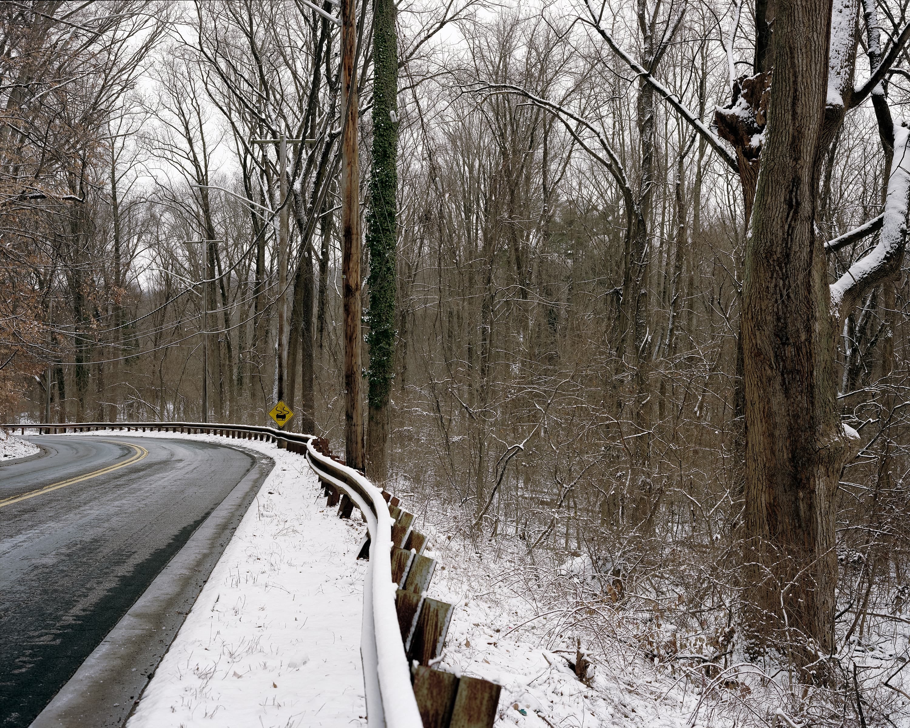 In winter, on a road passing through the historic park, a driving sign indicating sharp turns has been turned upside down.