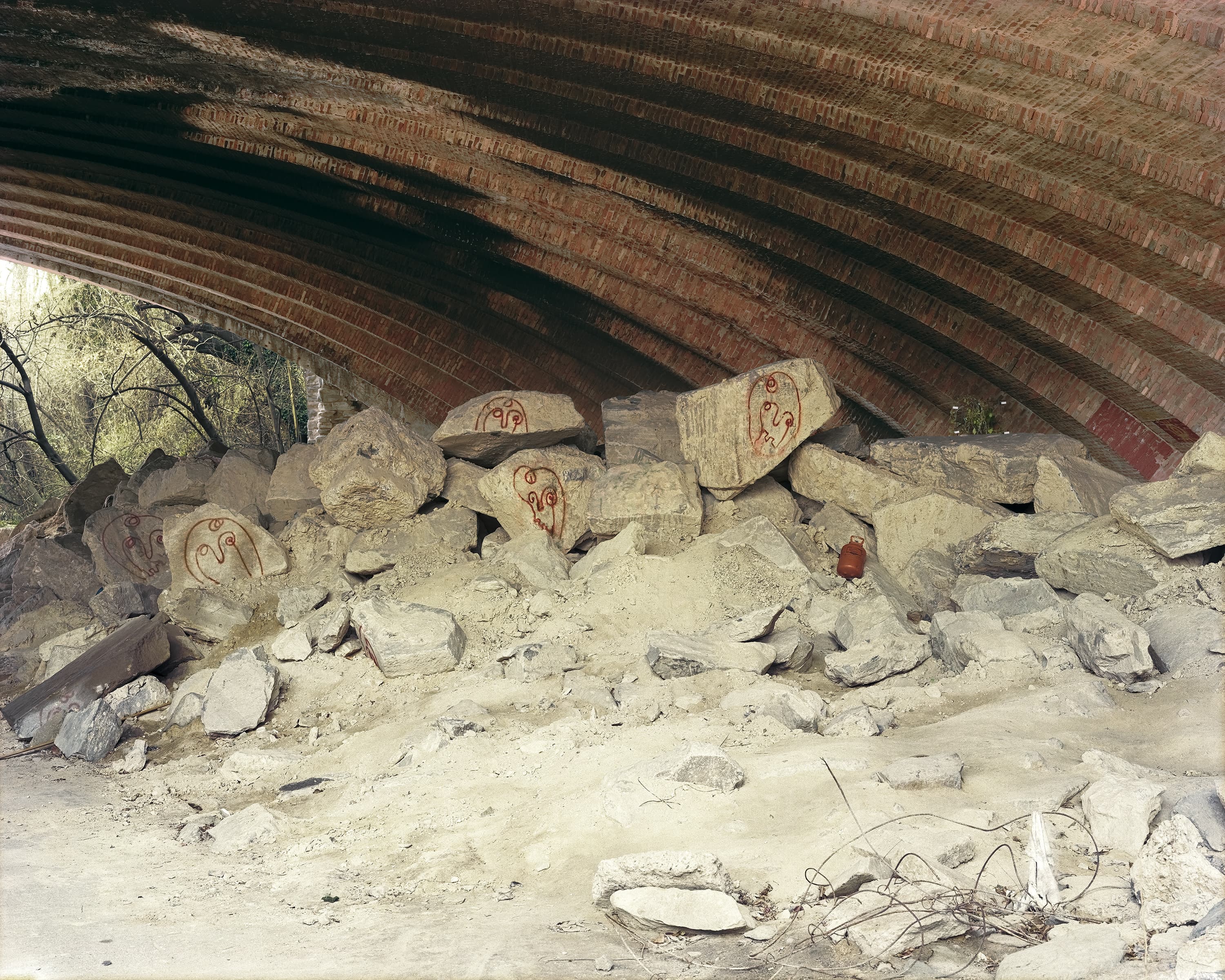 Painted heads on a large pile of rocks placed under historic bridge.