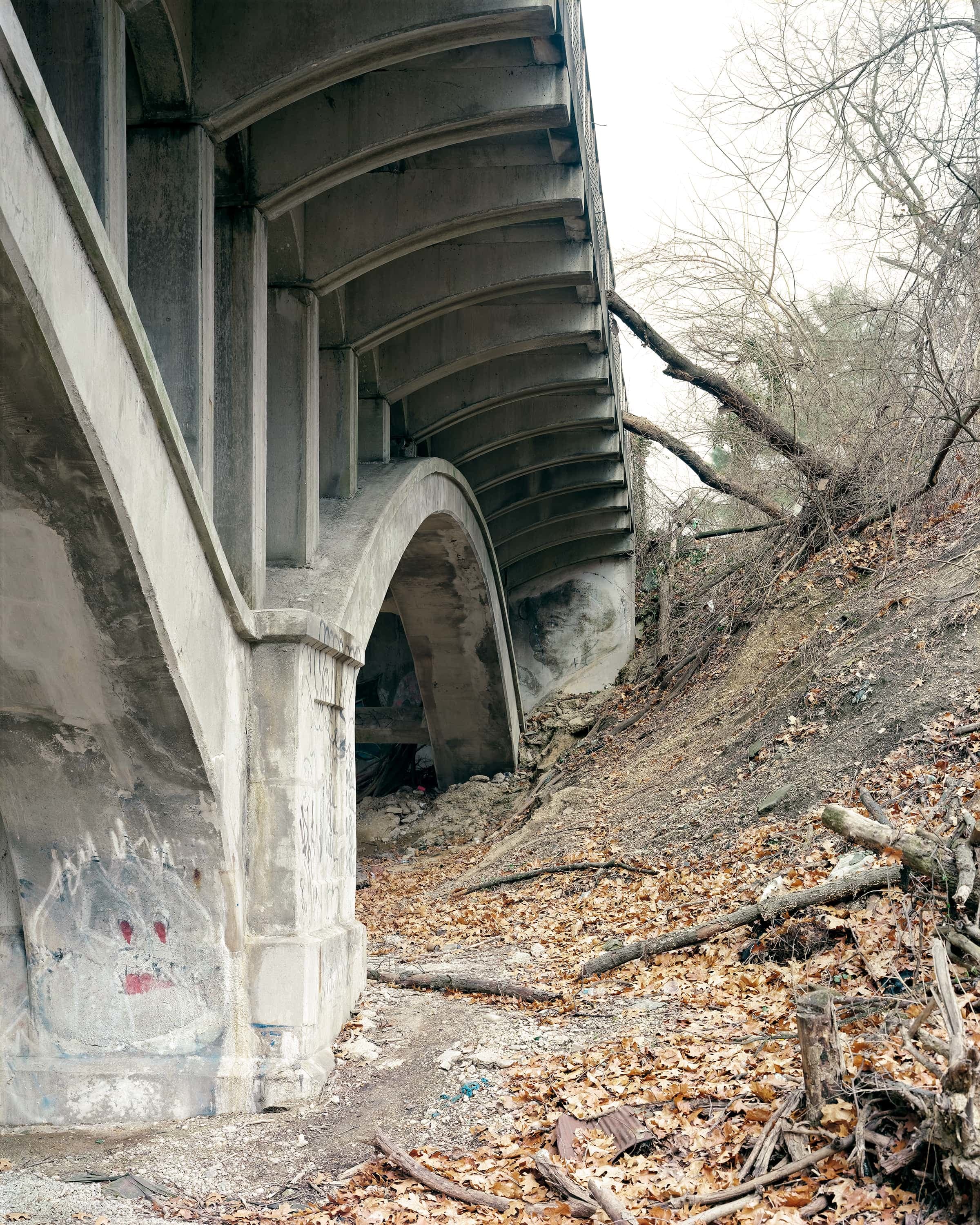 Looking under the arch of a bridge, a ghost is painted on the nearer pier a woman's head at on the pier further away.